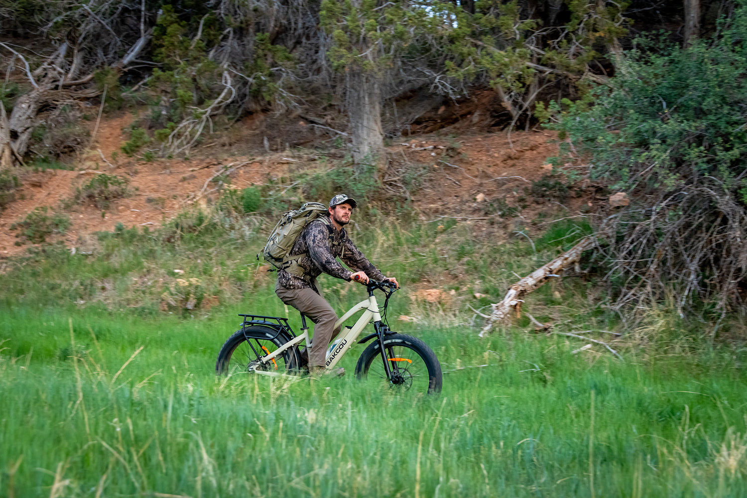 Hunter in camouflage with a backpack riding the Flatlander SD electric bike through tall grass, navigating rugged terrain with ease