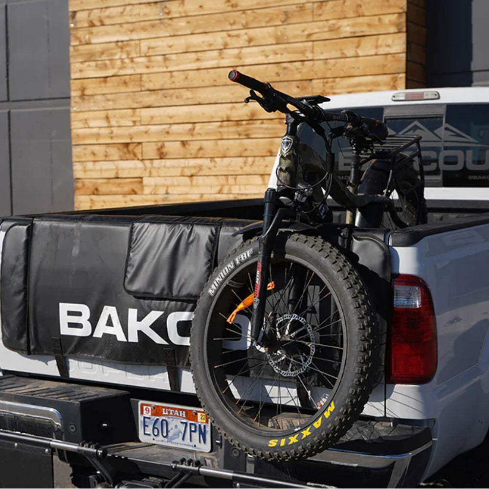 Bakcou Extendable Tailgate Pad installed on a truck, securely holding an electric bike for transport with durable straps and padded protection