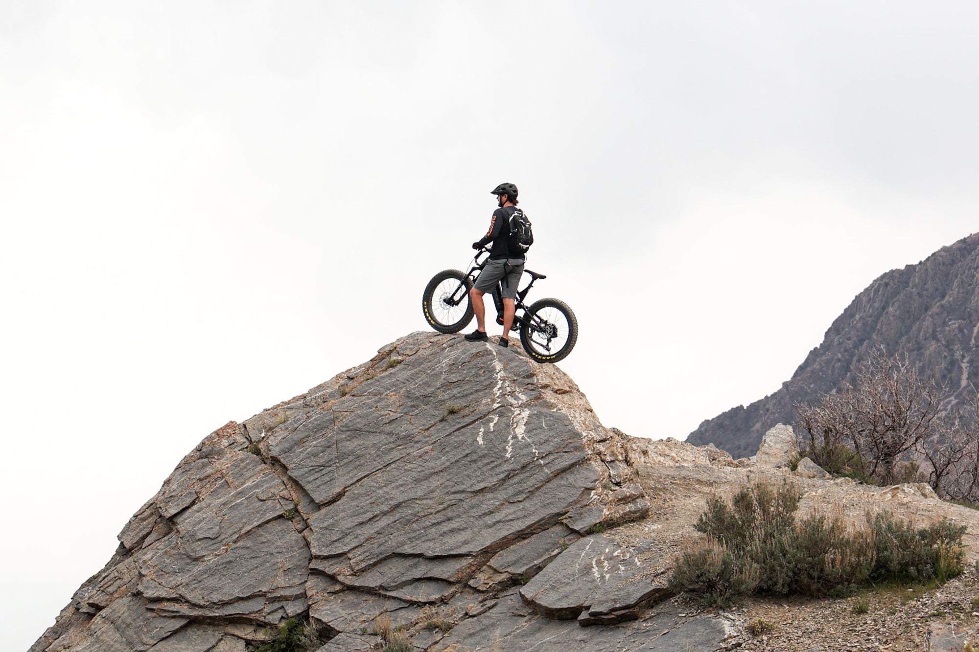 Bakcou Scout electric bike in matte black with man on top of steep rocky trail