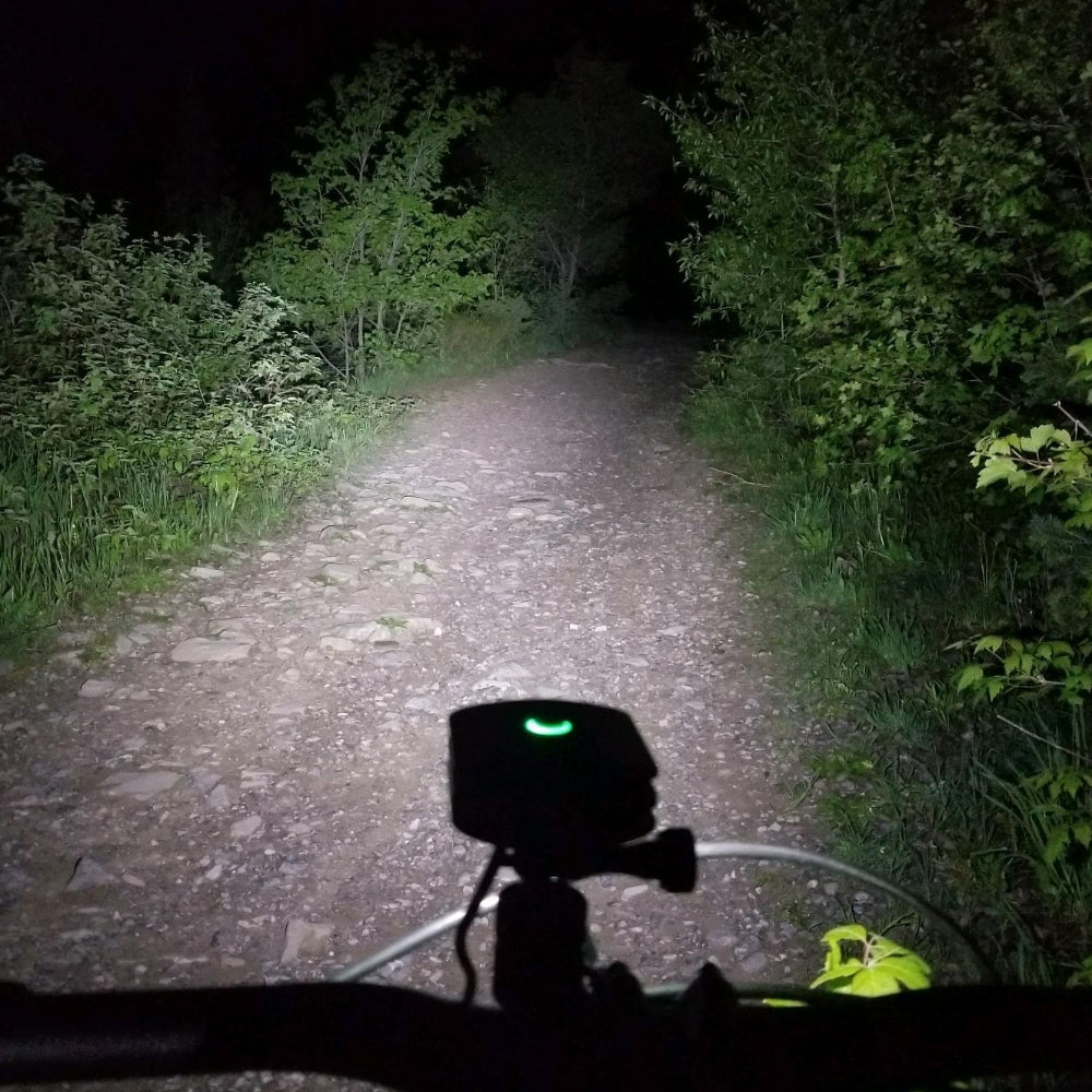 Bakcou 2200 Lumen Headlight illuminating a dark trail at night, demonstrating its high-powered flood beam for mountain biking and off-road riding.